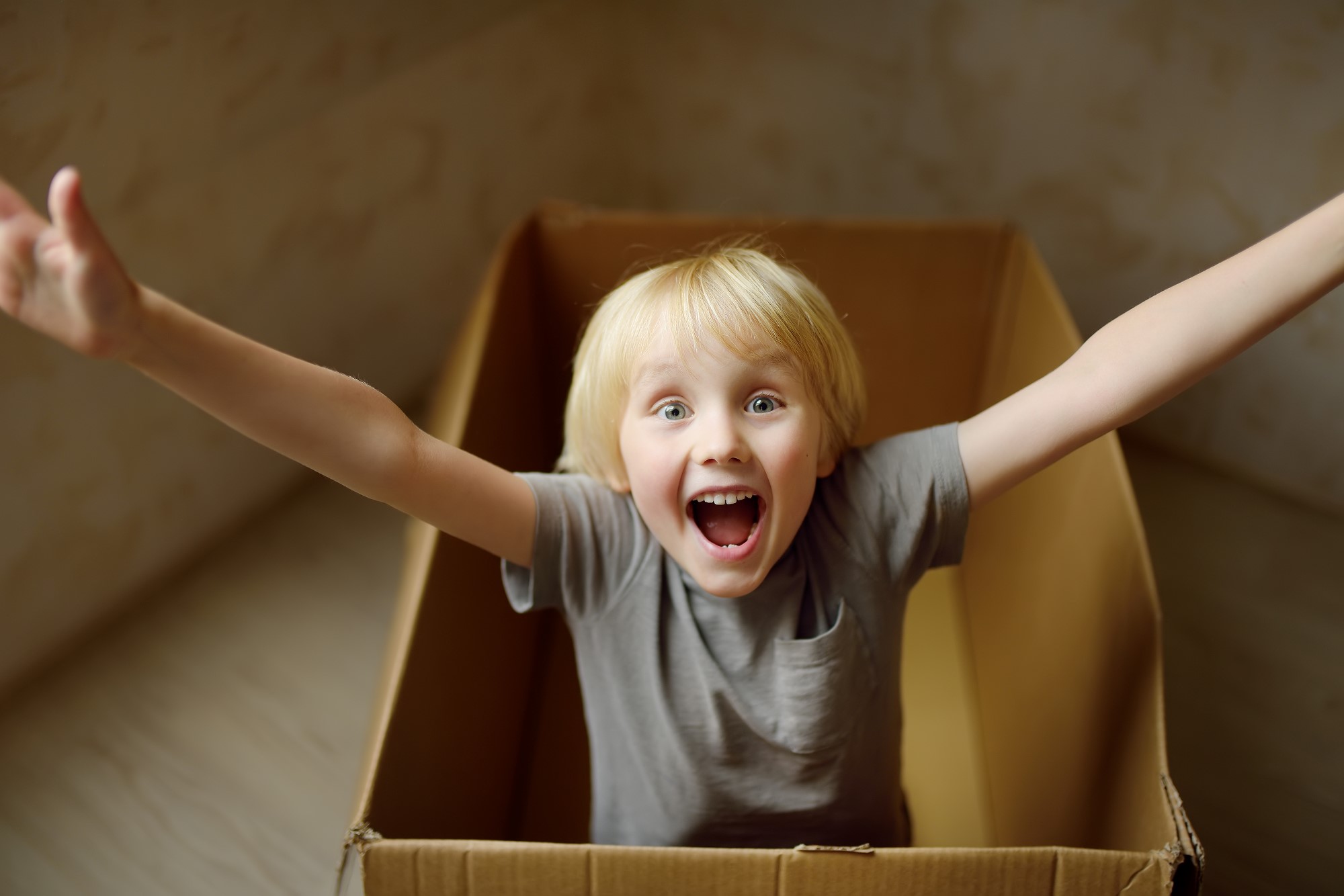 Cute preschool boy playing in a cardboard box during family's move to a new home. Kids play is a way of development of creative abilities.