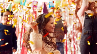 Group Of Children In Party Hats Celebrating At Birthday Party With Streamers And Gold Confetti